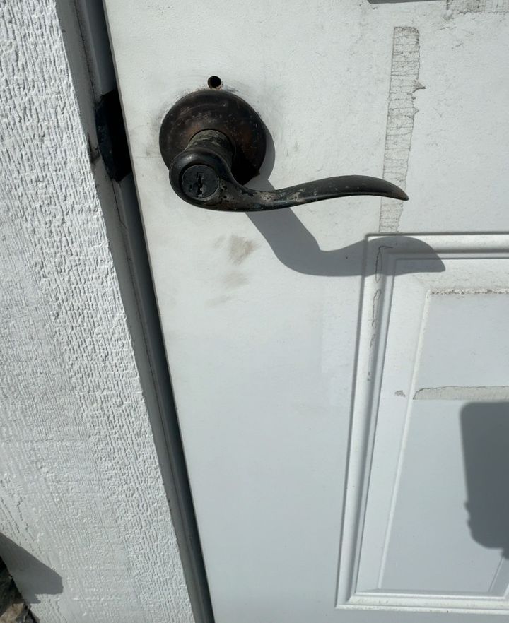 Weathered bronze entry lever on a white door before replacement, Boone NC
